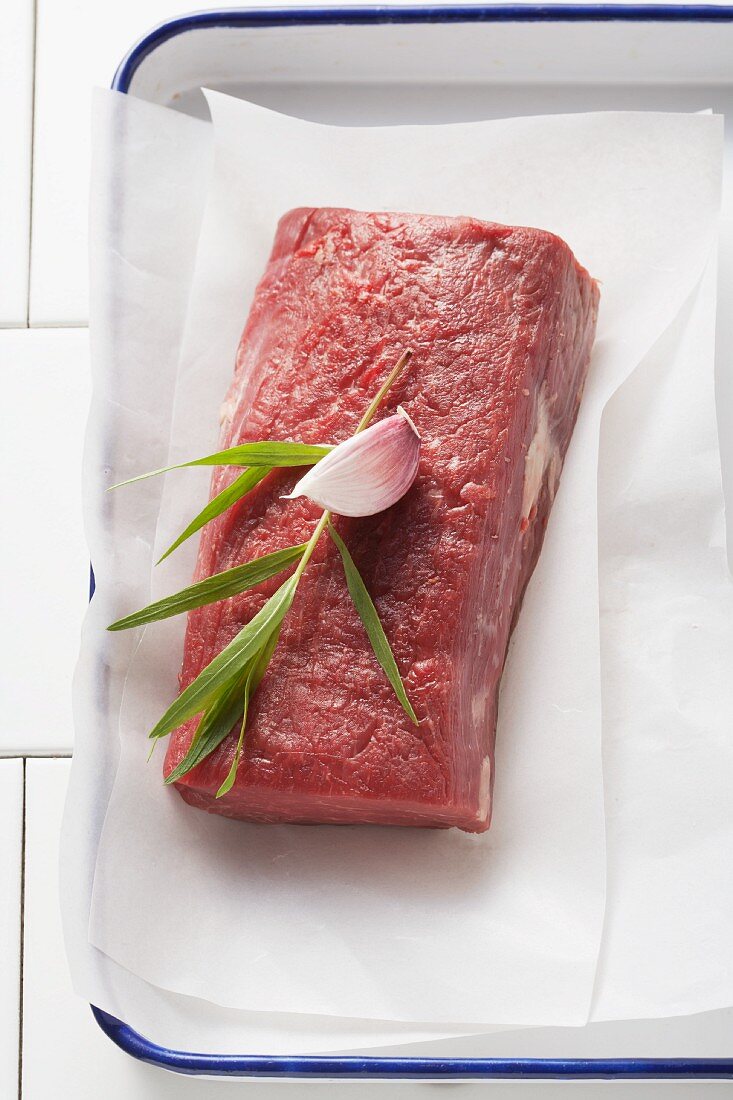A fillet steak with tarragon and garlic on parchment paper in a roasting tin