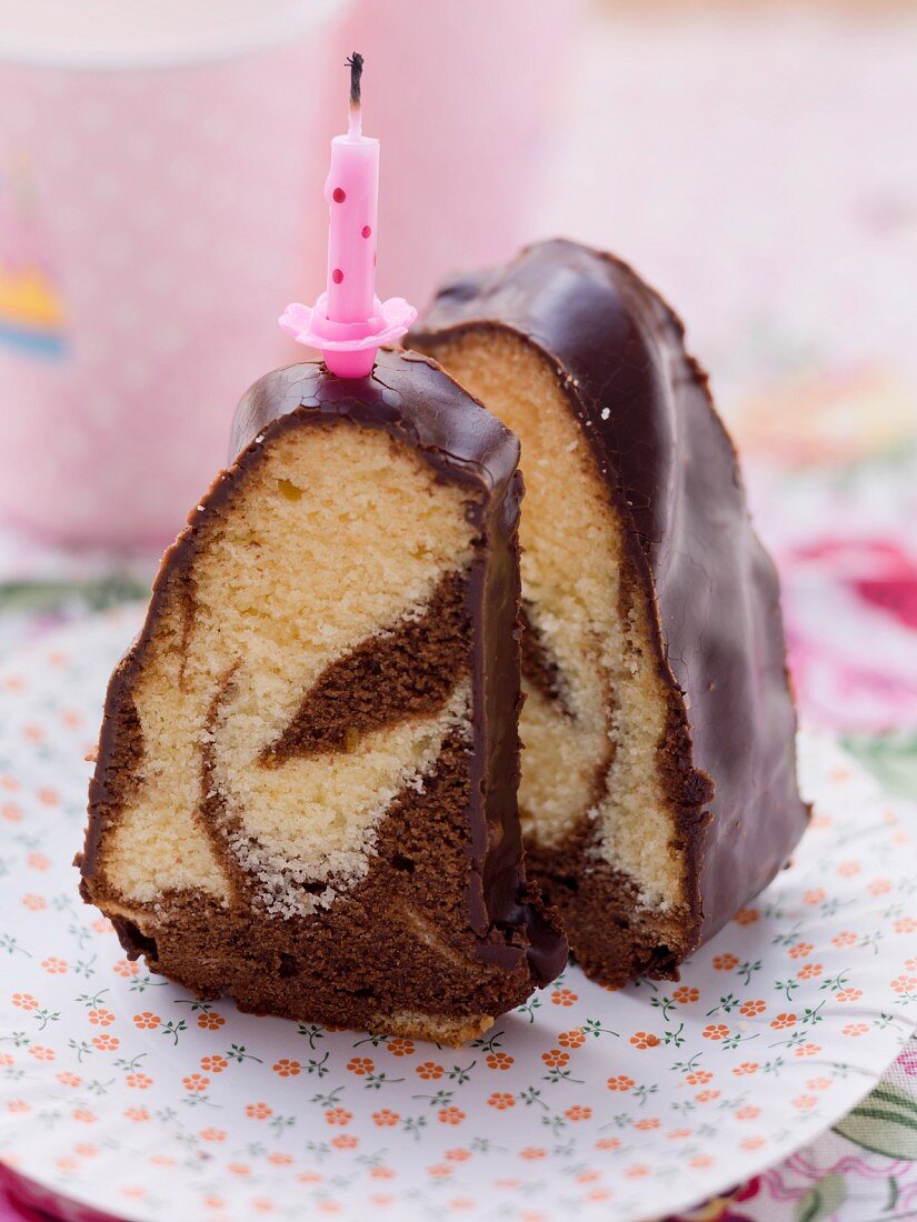 Two slices of marble cake with chocolate glaze and a birthday cake candle