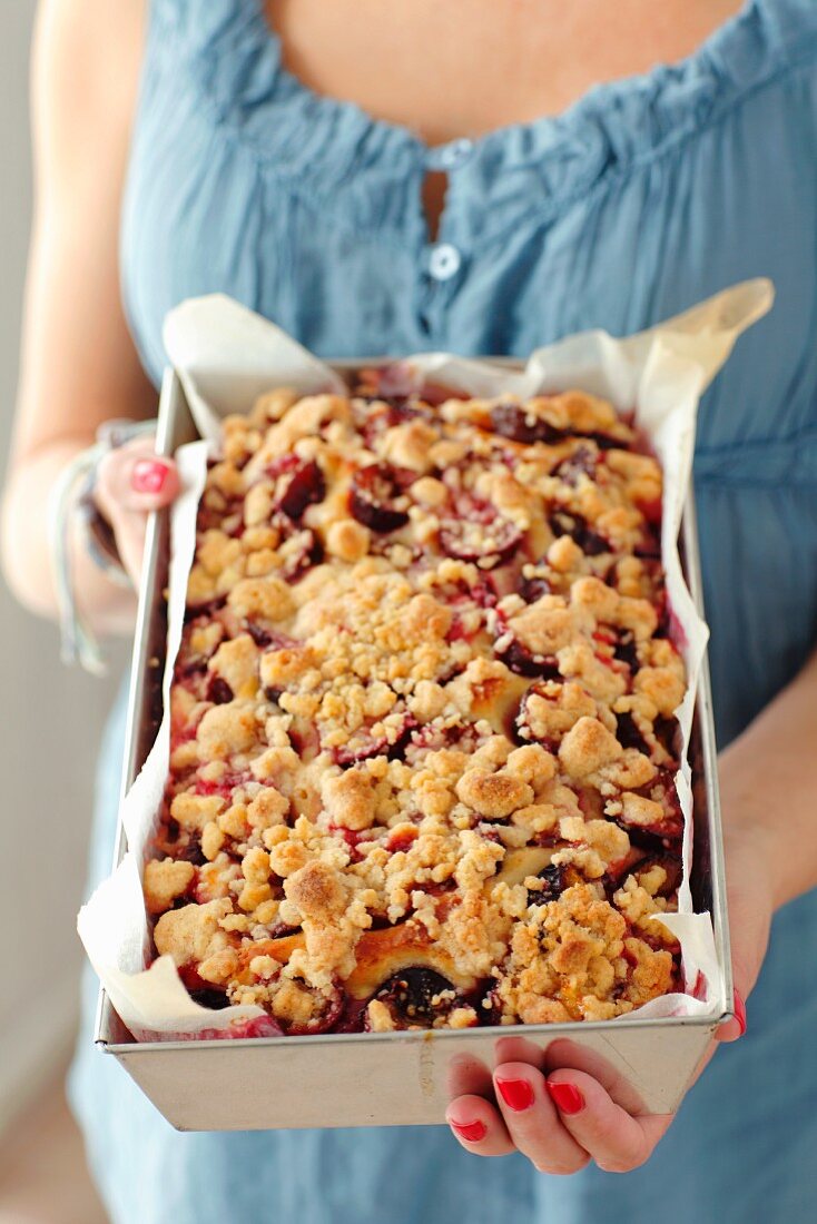 Frau hält Backform mit Pflaumen-Streusel-Kuchen