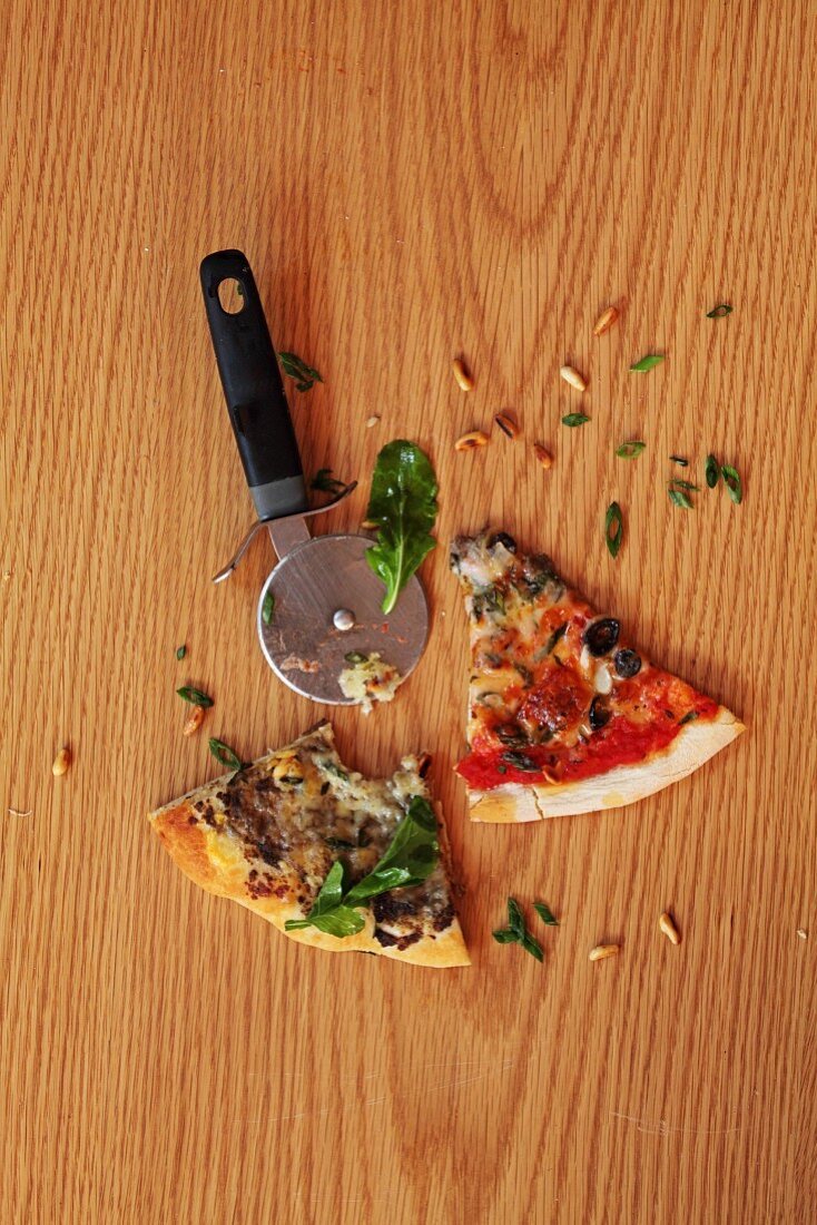Slices of pizza and a pizza wheel on a wooden surface