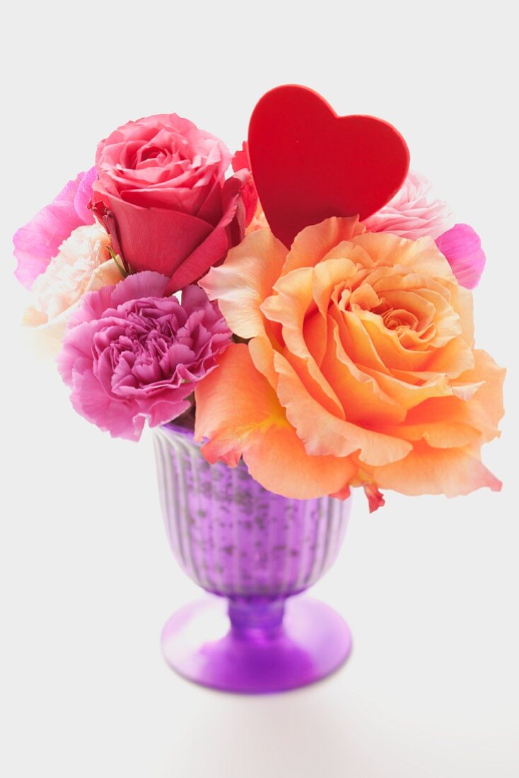 Various flowers and a heart in a purple vase