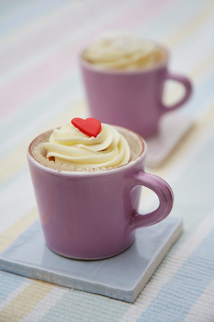 A cupcake decorated with light frosting and a marzipan heart in a cup