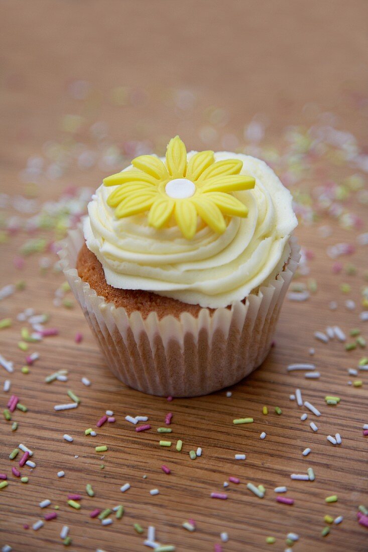 A cupcake decorated with light frosting and a marzipan flower
