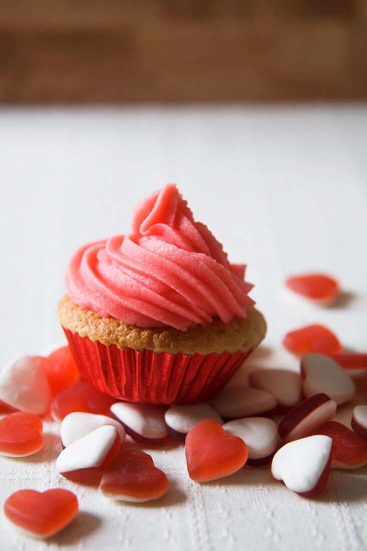 A Cupcake with Pink Frosting Surrounded by Candy Hearts