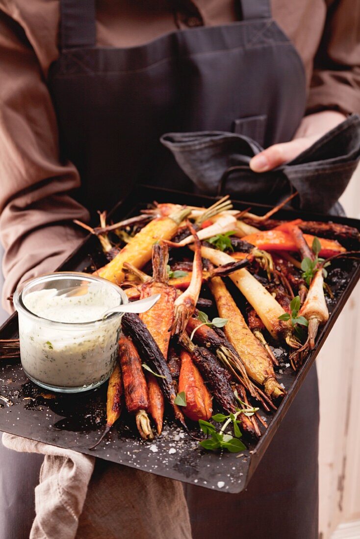 Root vegetables on a baking tray with a herb dip
