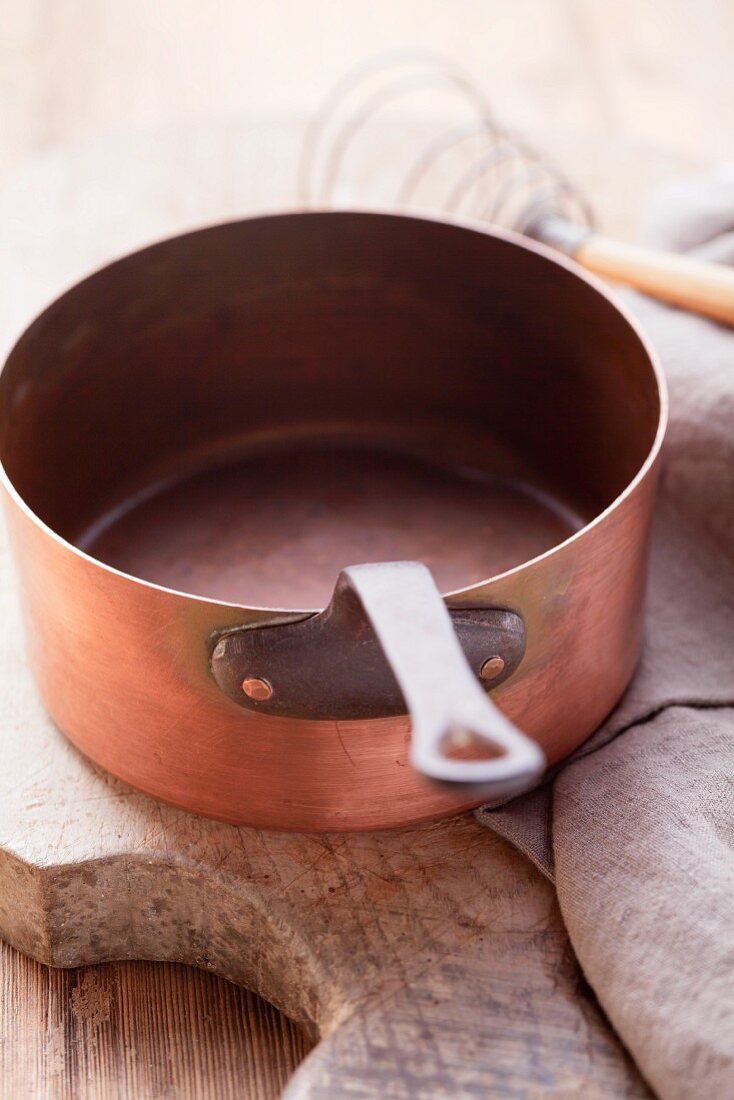 A copper saucepan on a wooden board