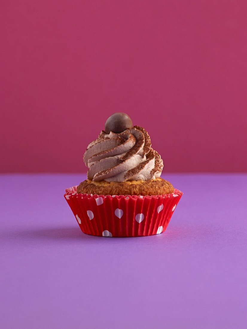 A cupcake on a purple surface against a pink background