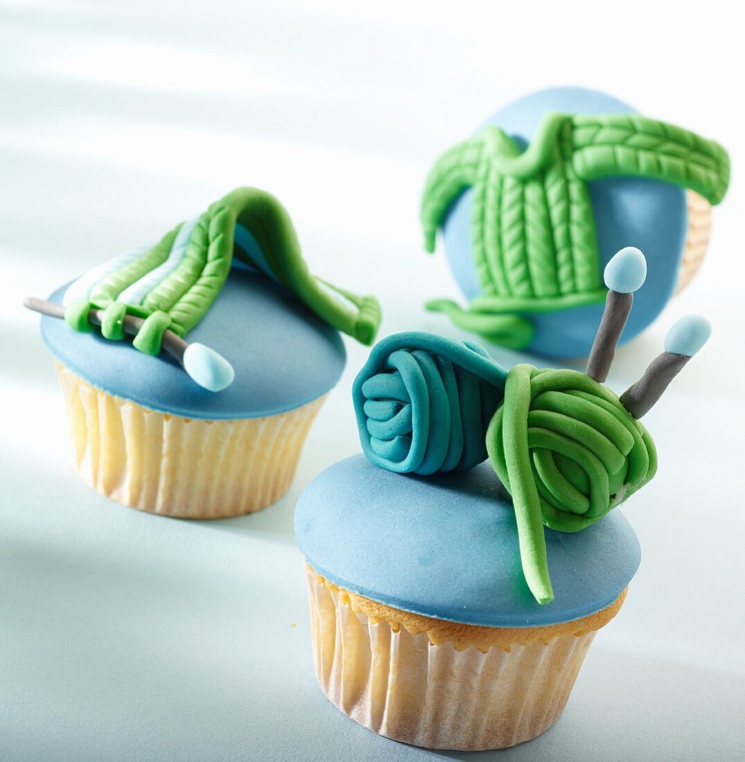 Three cupcakes with blue icing and marzipan knitting decorations