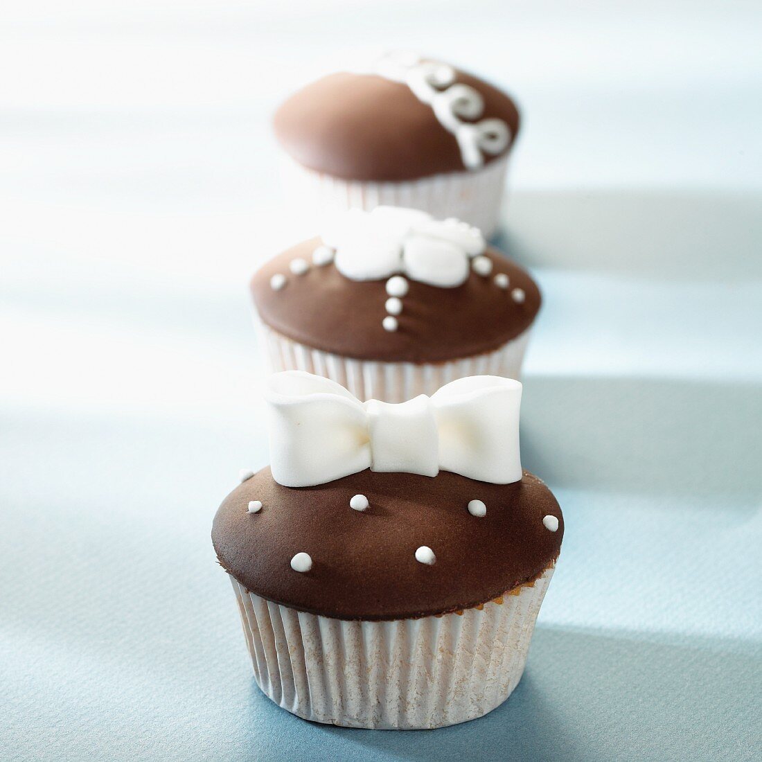 Three cupcakes with brown and white decorations