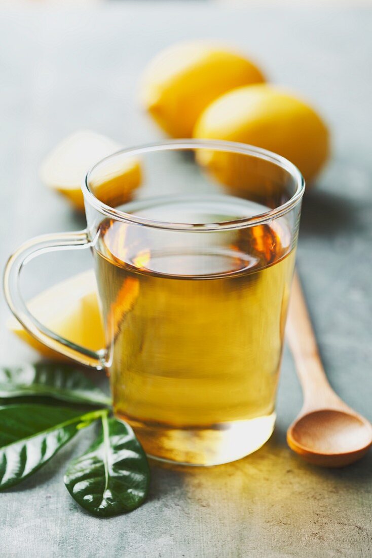 Ein Glas mit Tee, im Hintergrund Zitronen