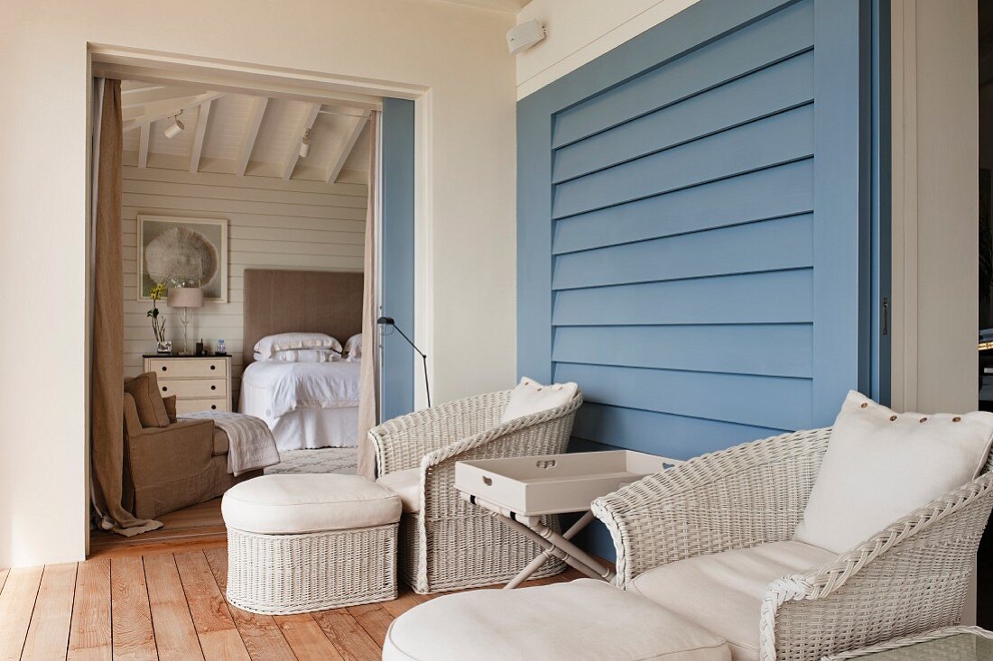 Bequeme Balkonmöbel mit Fussschemel und Tabletttisch vor blauer Wand und Blick ins Schlafzimmer durch die geöffnete Schiebetür