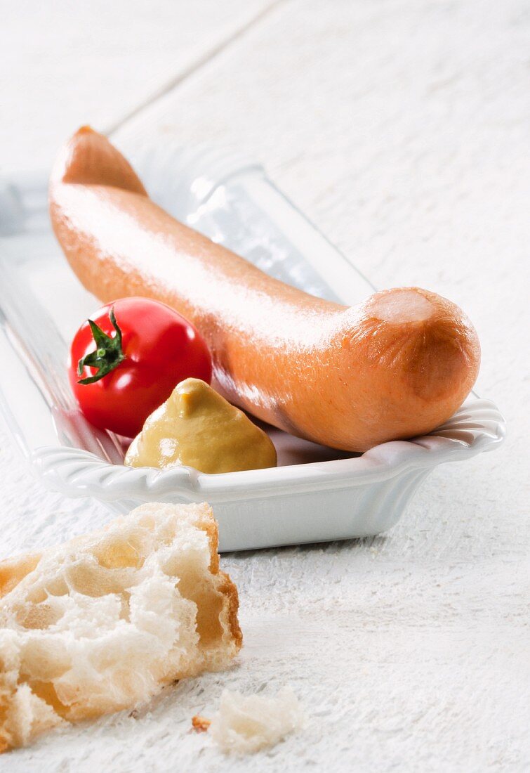A hot dog sausage with mustard, a tomato and bread