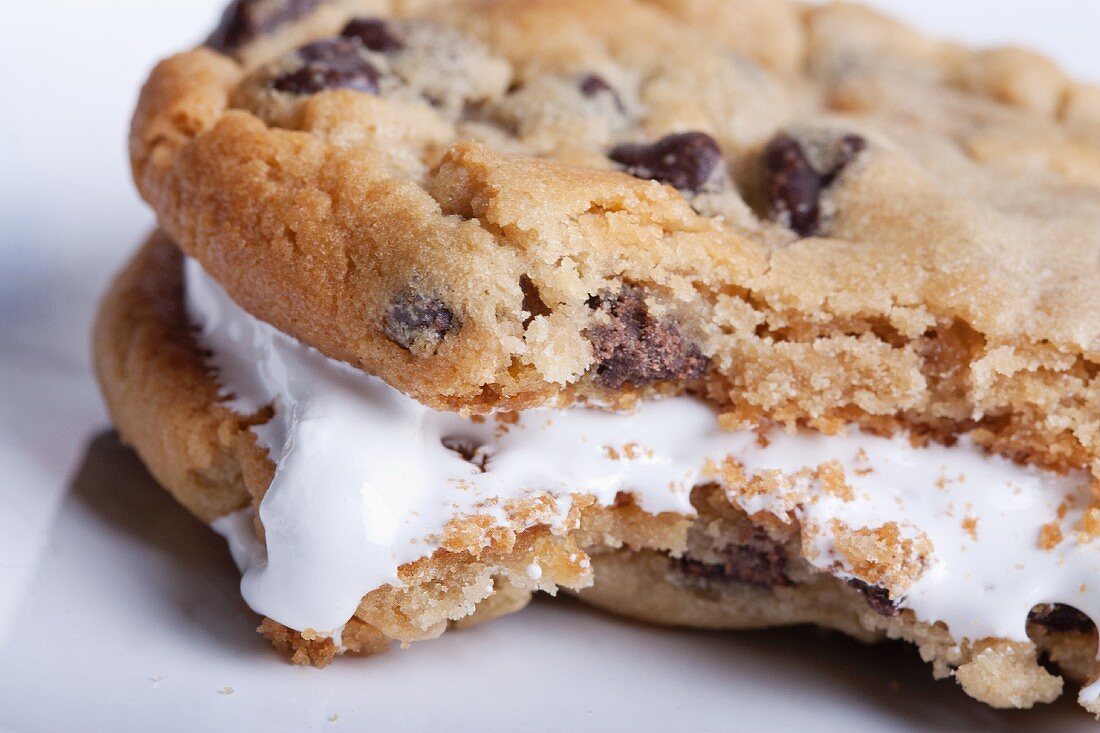A chocolate chip sandwich cookie filled with cream with a bite taken out of it