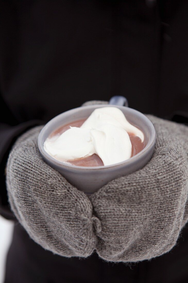 Gloved hands holding hot chocolate with cream