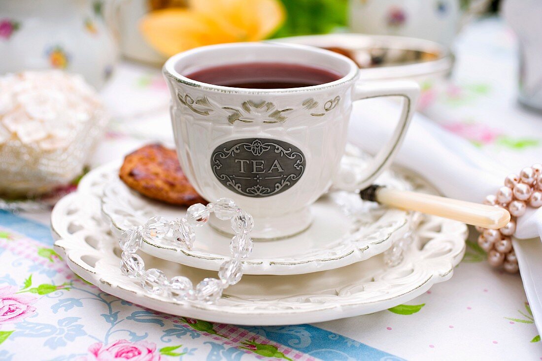 A cup of tea with a tea biscuit on a decorative table