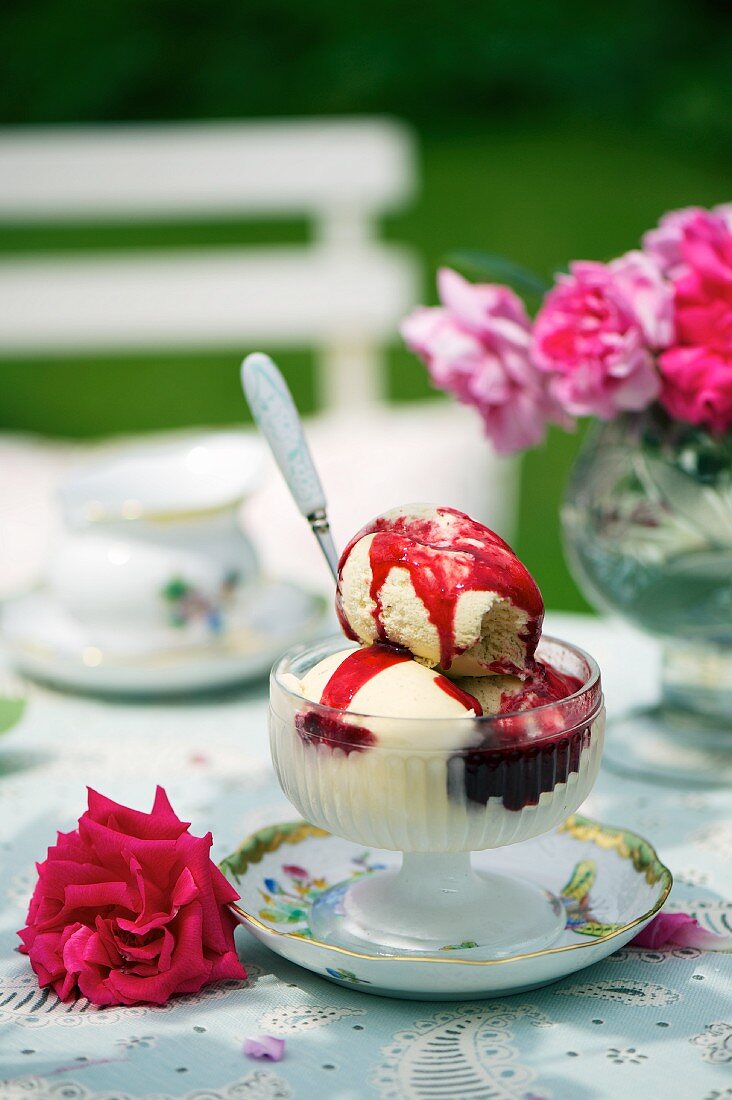 Vanilla ice cream with berry sauce on a table in the garden