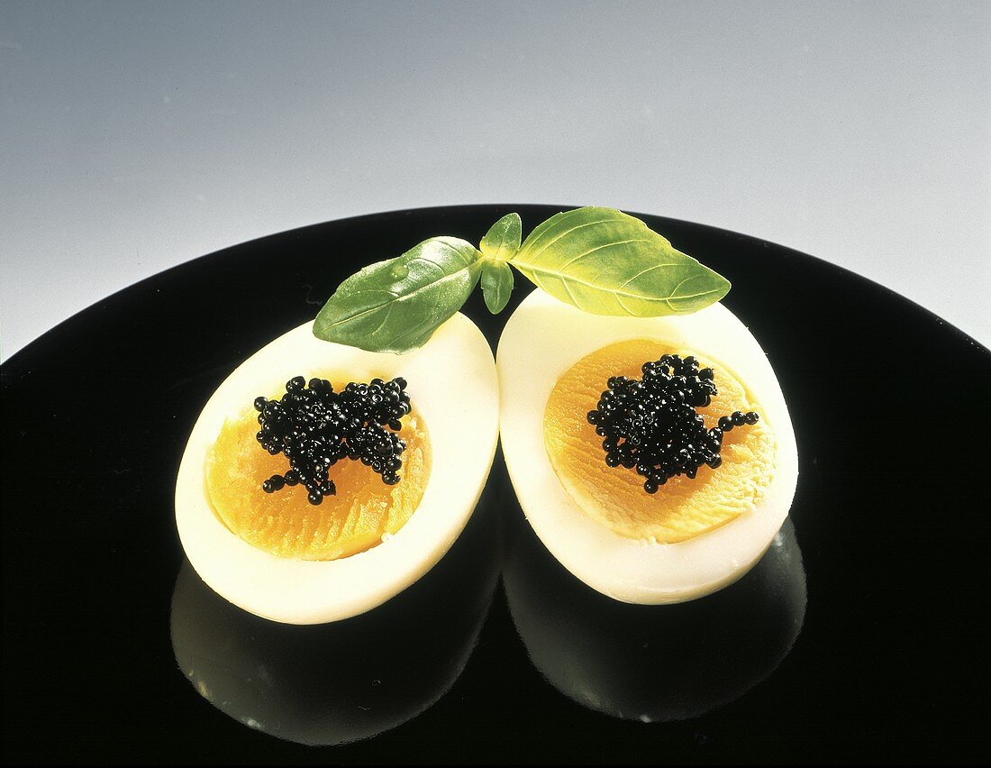 Gekochtes, halbiertes Ei mit schwarzem Kaviar; Deko-Basilikum