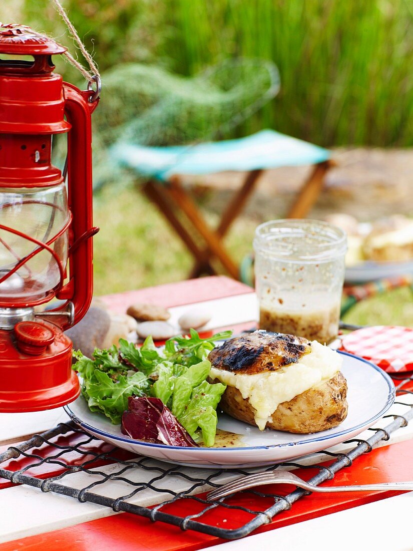 Potato baked in the barbecue, with cheese filling, on a table outdoors