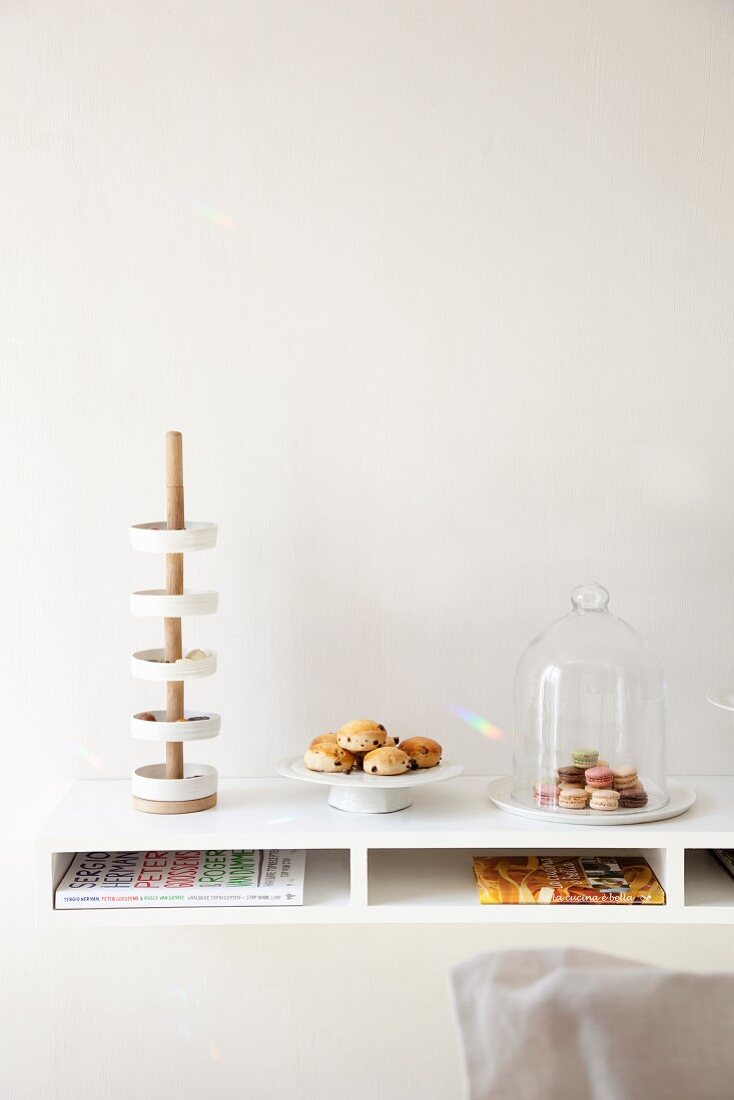Modern cake stand made from dishes on wooden pole, small plate of pastries and glass cover