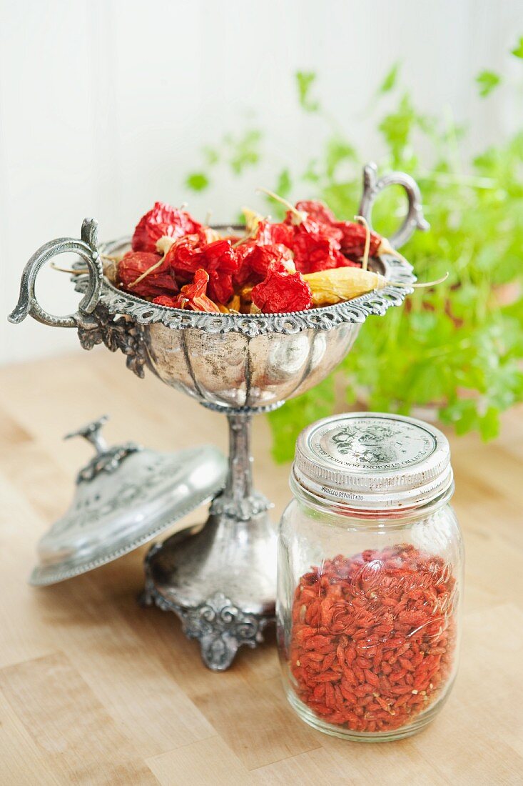 Getrocknete Chilischoten in Silberschale und Gojibeeren im Glas