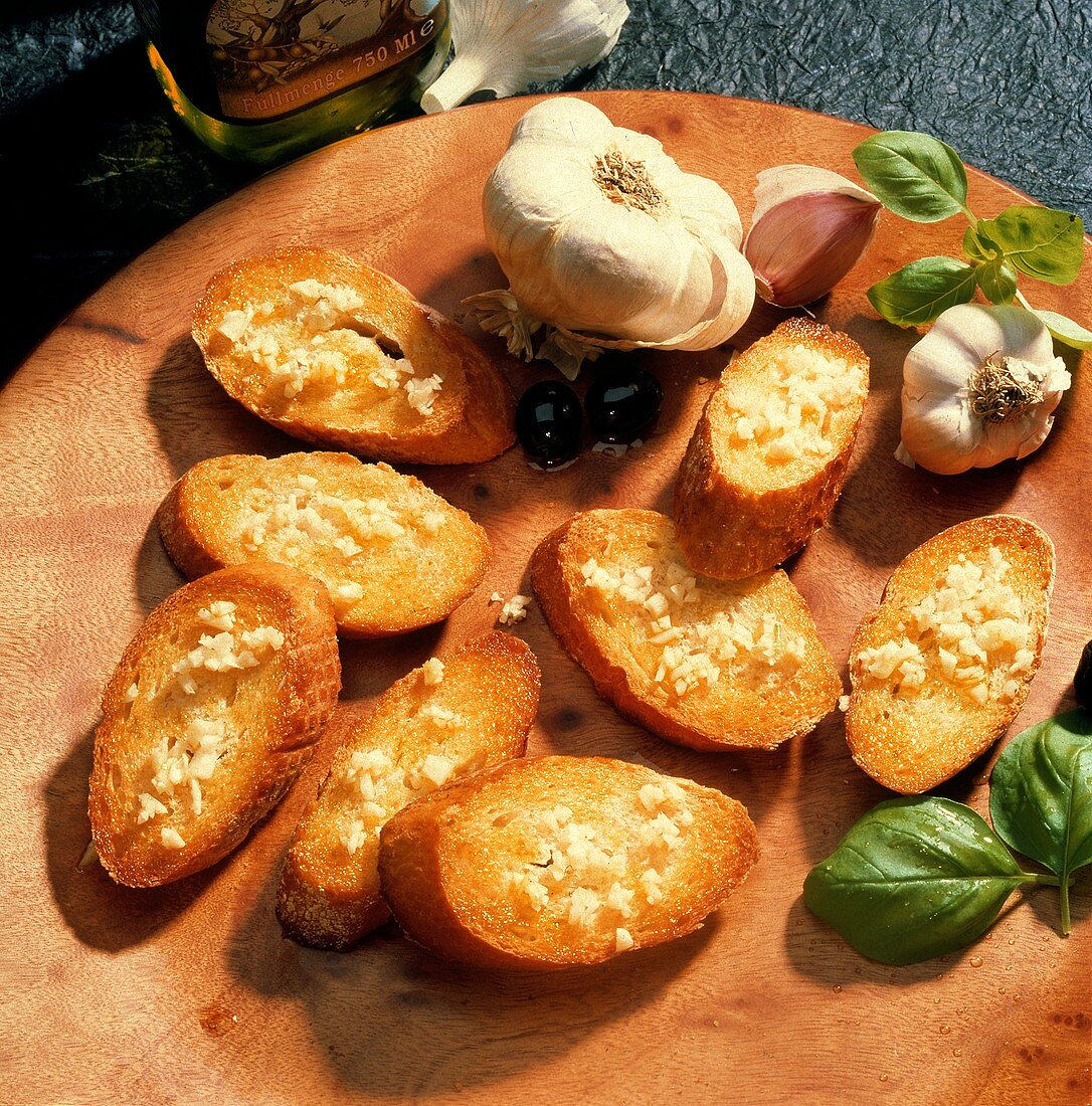 Roasted Garlic Bread on round wooden Board with fresh Garlic, Basil and black Olives