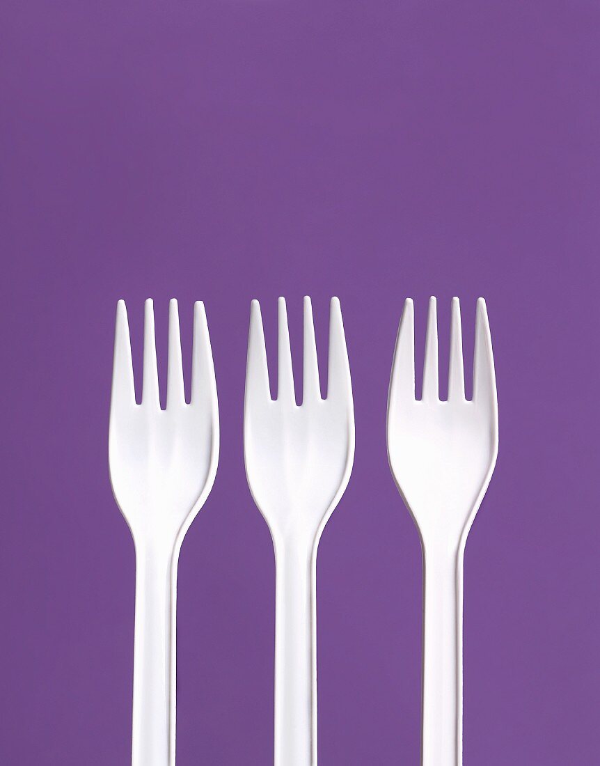 Three White Plastic Forks on a Purple Background