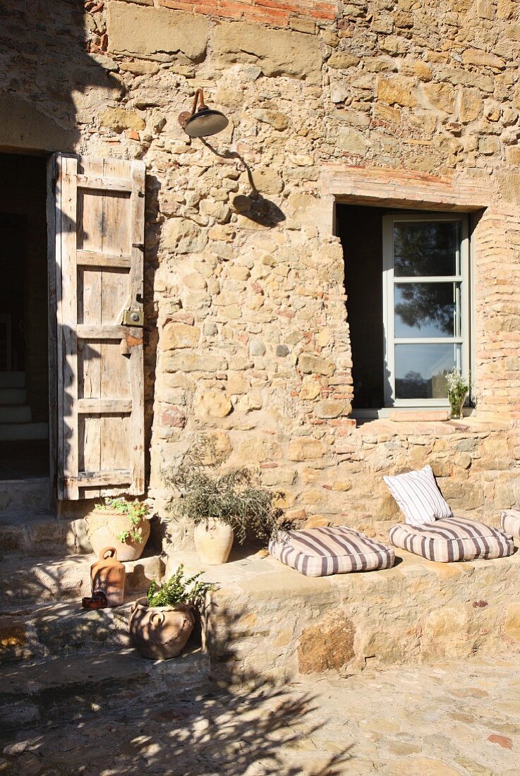 Cushions on stone bench below window on outside wall of Mediterranean stone house