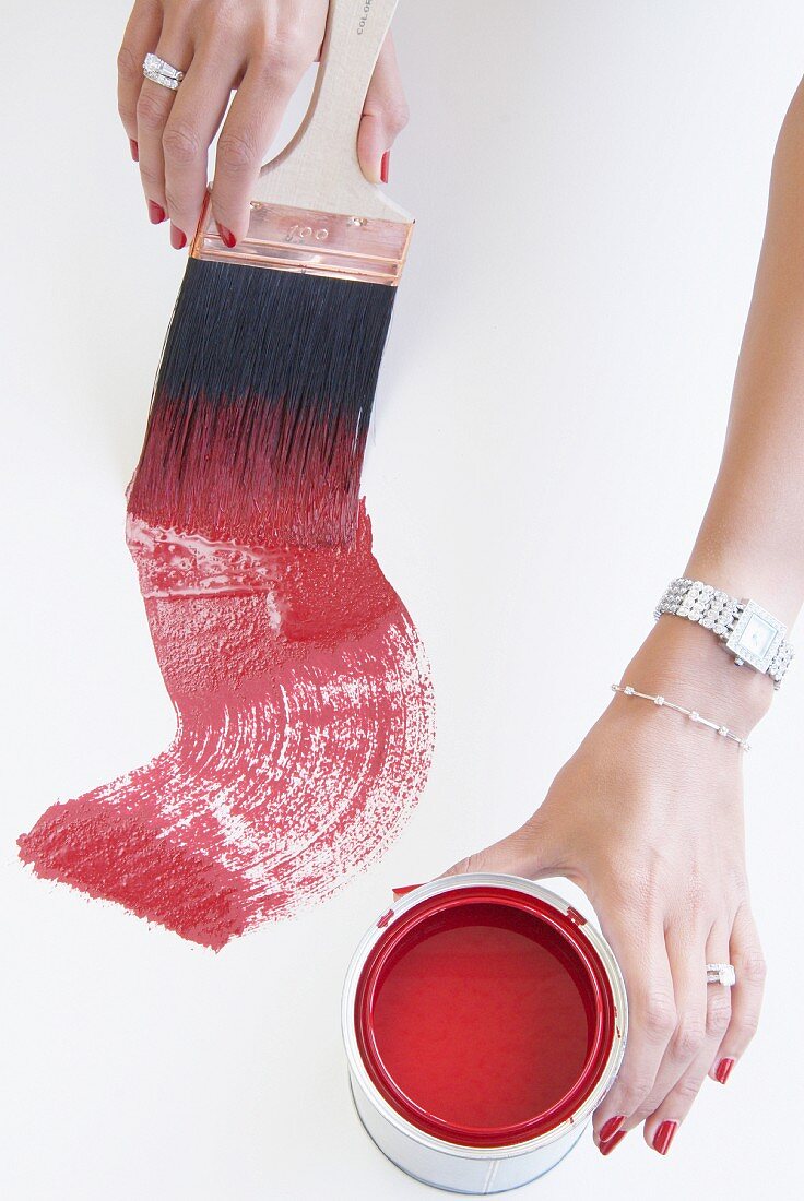 Gepflegte, mit Schmuck behangene Frauenhände bei der Arbeit mit roter Farbe und Pinsel