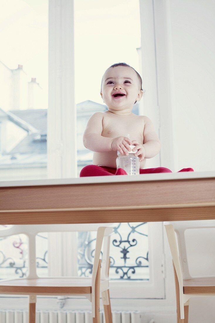 Laughing baby with its bottle sitting on a table