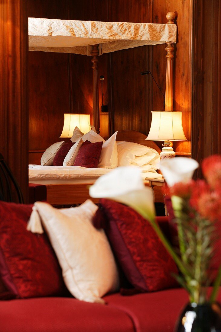Romantisches Hotelbett auf Schloss Schauenstein mit Baldachin im Antikstil; Kissen auf Sofa verschwommen im Vordergrund