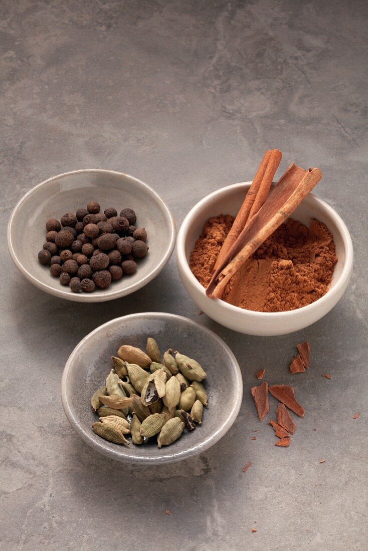 Three dishes of spices: allspice, cardamom and cinnamon