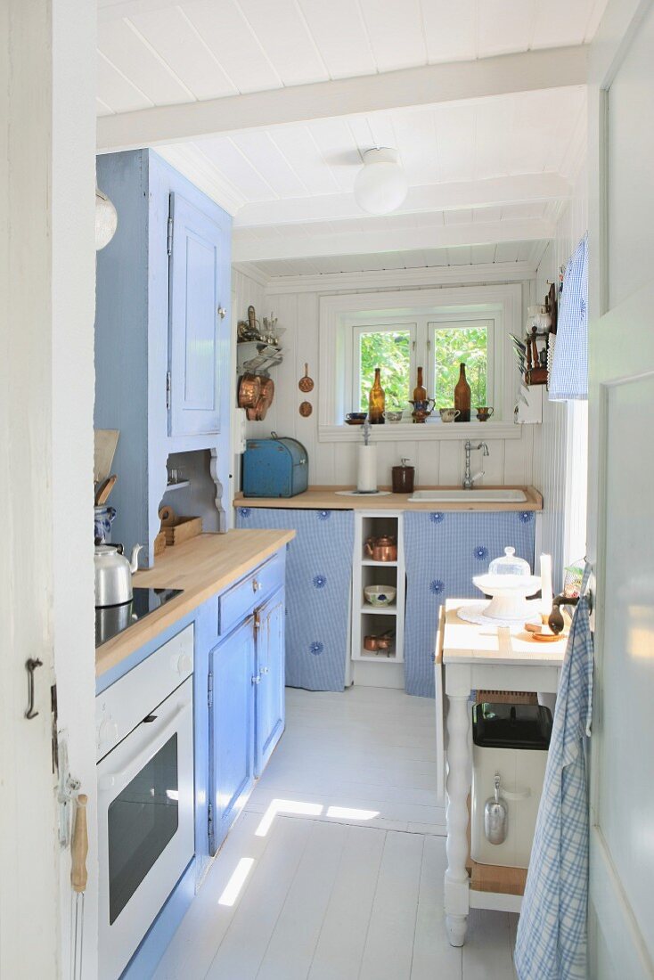 Cheerful kitchen in pastel blue with white tiled floor and pale wooden surfaces