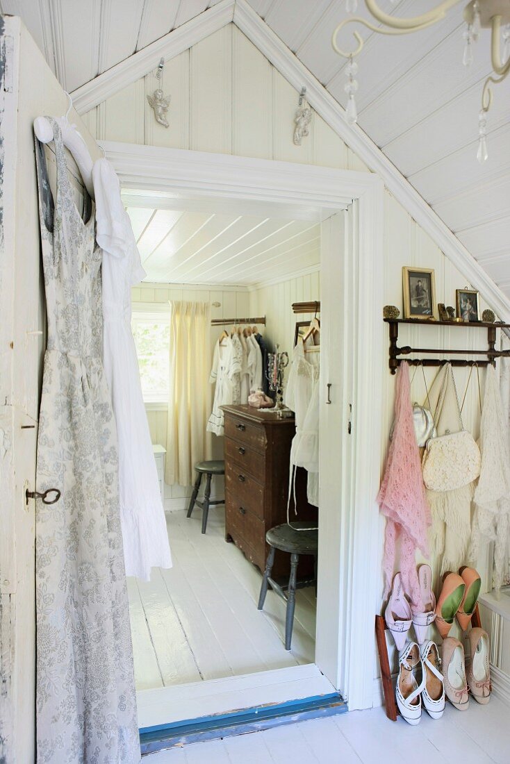 Antique chest of drawers and vintage chairs in attic dressing room with summer shoes on shoe rack in foreground