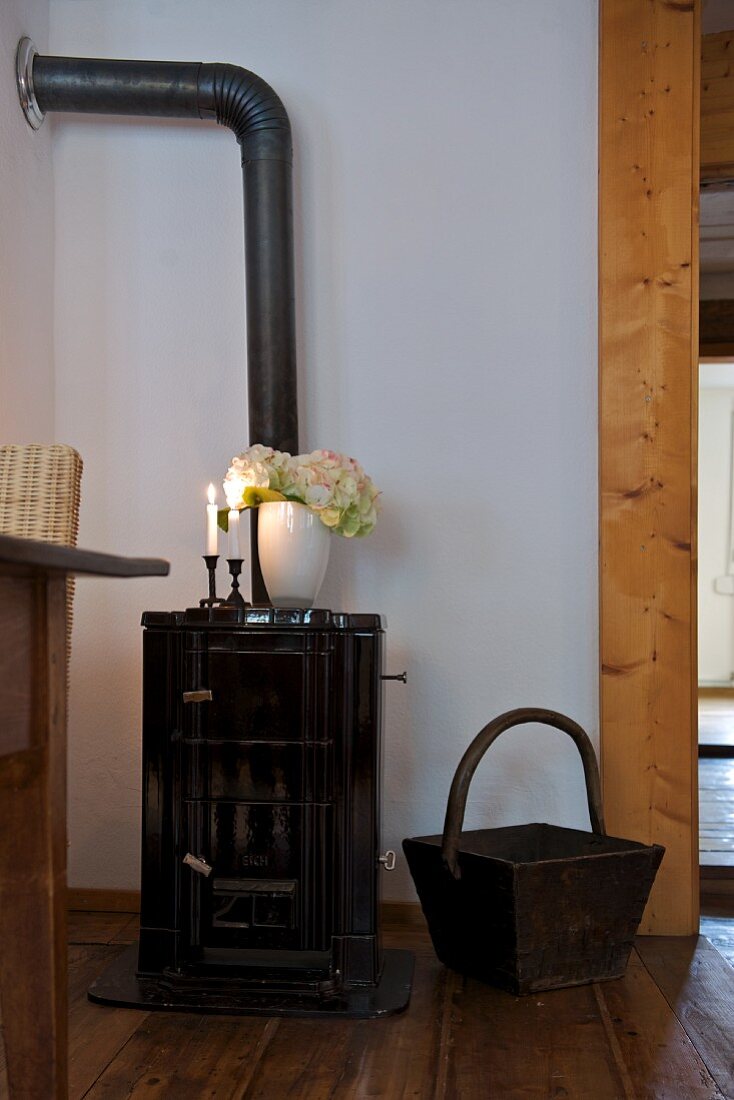 Vase of flowers and lit candles on old wood-burning stove in renovated house