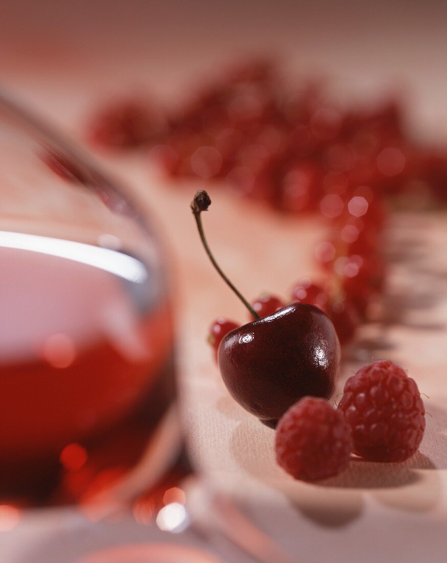 A glass of red wine with raspberries, cherries and redcurrants