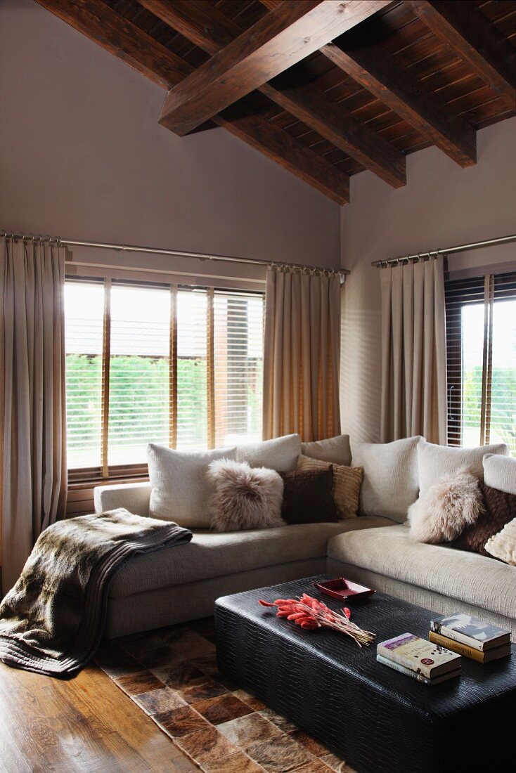 Cozy, fur look accessories on a bright, corner sofa and black ottoman under an impressive wood beam ceiling