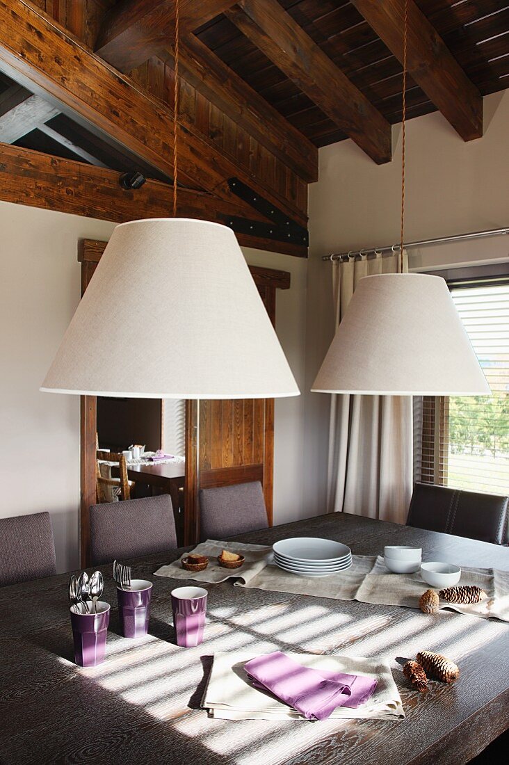 Zwei konische Lampenschirme über Esstisch und offene Dachkonstruktion aus Holz