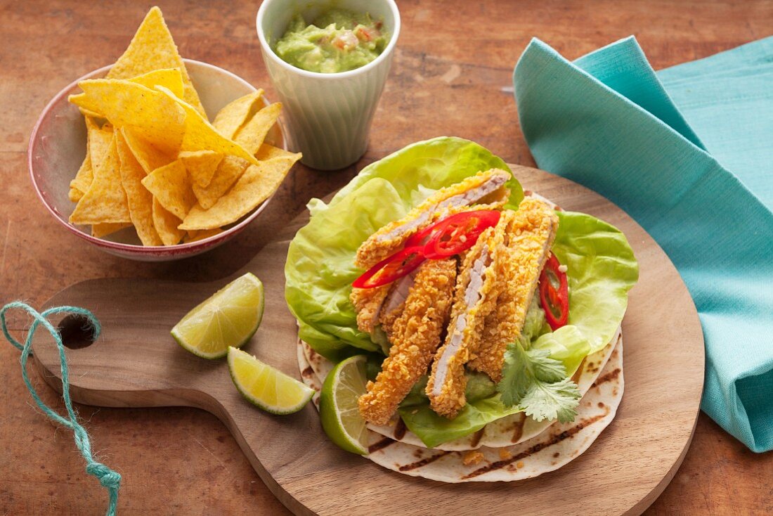 Strips of schnitzel in a nacho crumb coating, guacamole and tortillas