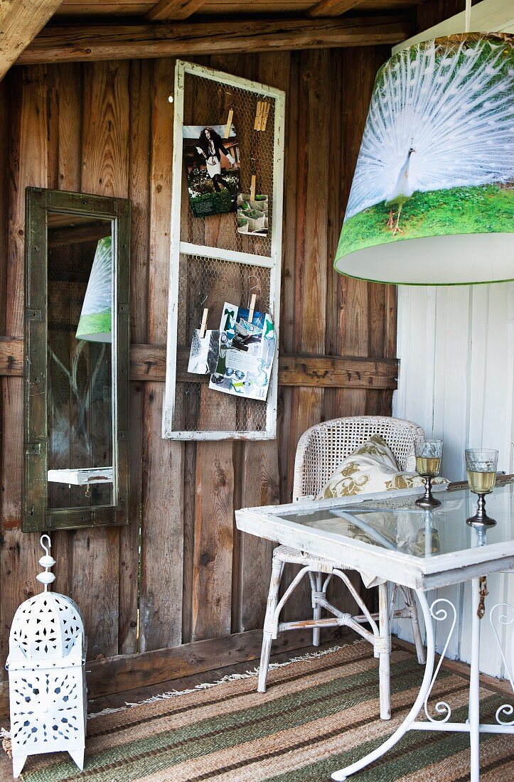 Pictures pegged to chicken wire and mirror on wall next to chair and table on rustic wooden terrace