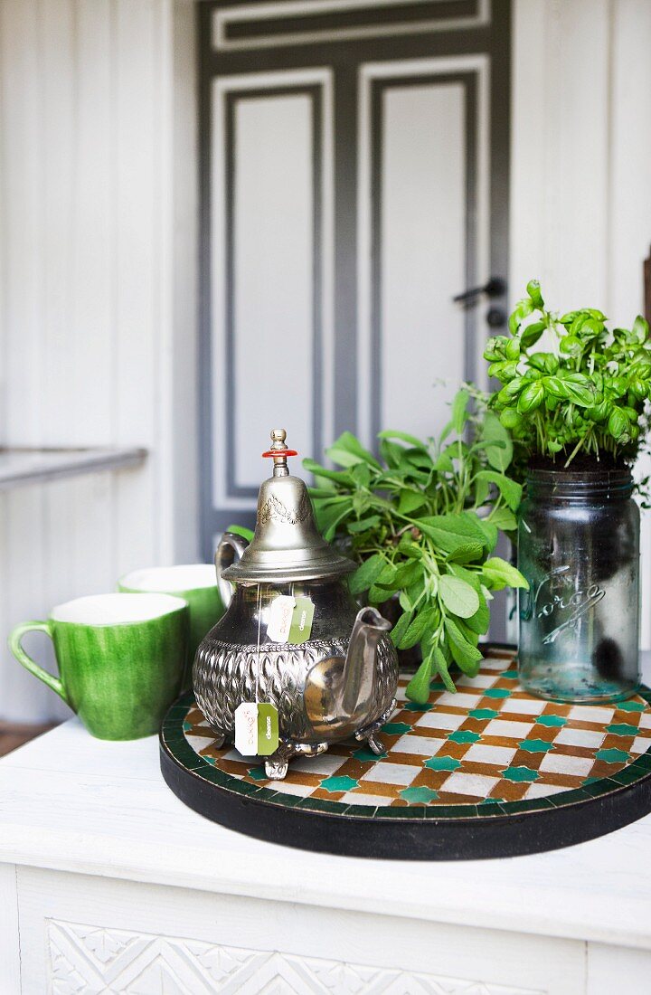 Sage, basil and silver teapot on tiled mosaic tray