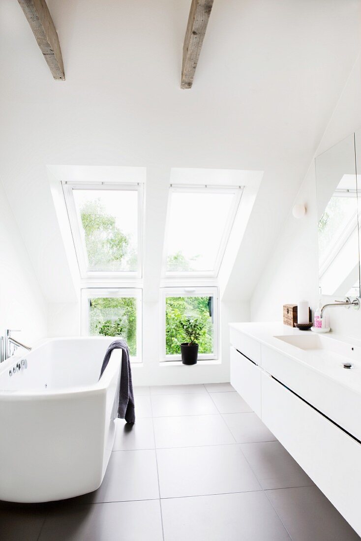 Modern bathtub opposite washstand with integrated sink in designer bathroom with dormer window