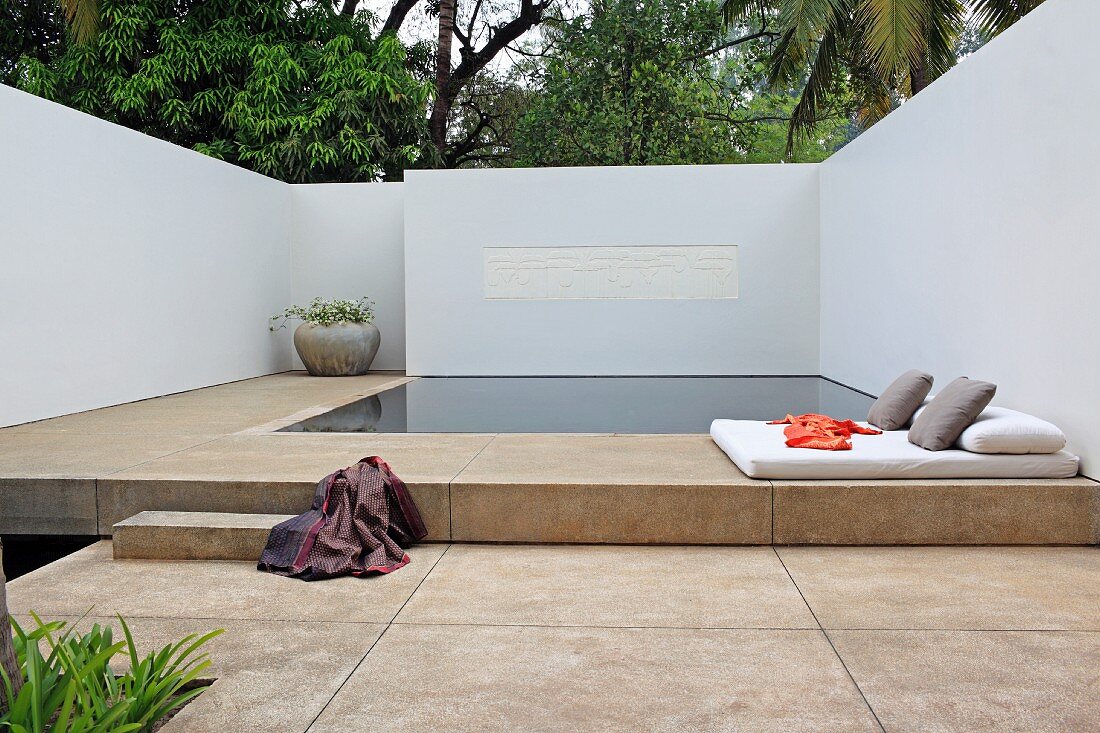 Quiet and serene geometric pool area with floor cushions and pillows surrounded by white walls overhung by trees