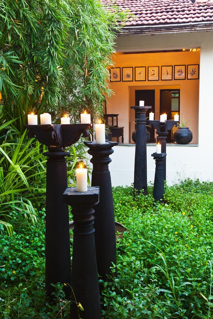 Lit candles on black, floor-standing candlesticks in garden