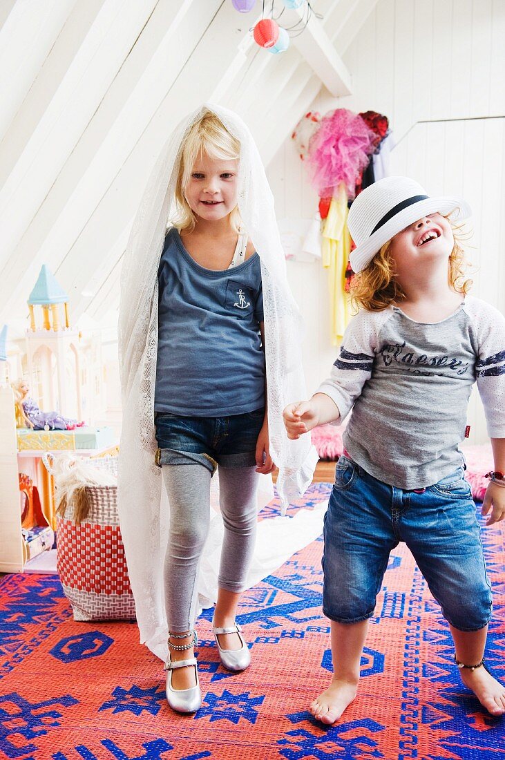 Two little girls playing dress-up on blue and red kilim rug; attic room with white-painted wood panelling