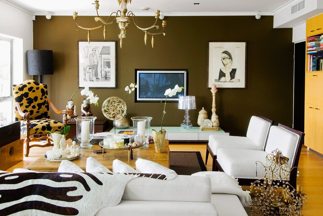 Sitzgruppe mit Animalprint und Opiumtisch in elegantem Wohnzimmer; gerahmte Bilder an schokobrauner Wand im Hintergrund