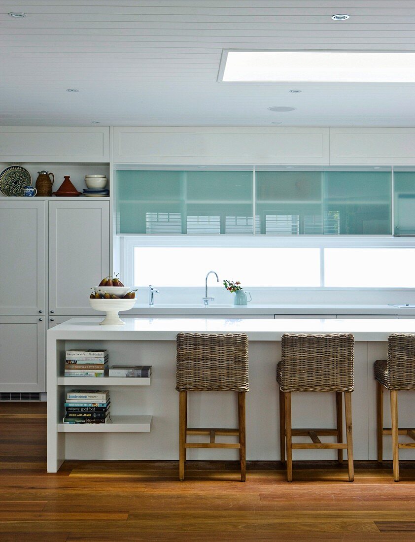 White fitted kitchen with modern fronts, vintage cupboard and wicker chairs at kitchen counter