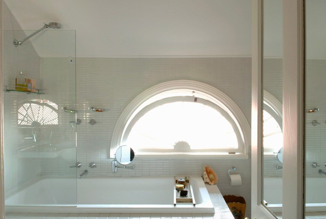 Bath and shower with glass screen in front of semi-circular window in bathroom