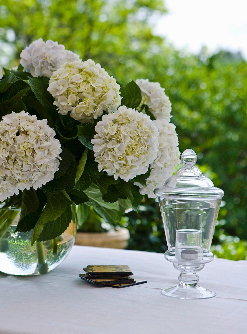 Outside: bouquet of hydrangeas and chalice shaped outdoor glass candle holder on a table set in white