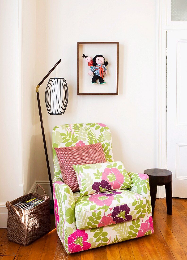 Comfortable armchair with cheerful floral upholstery and retro standard lamp in corner