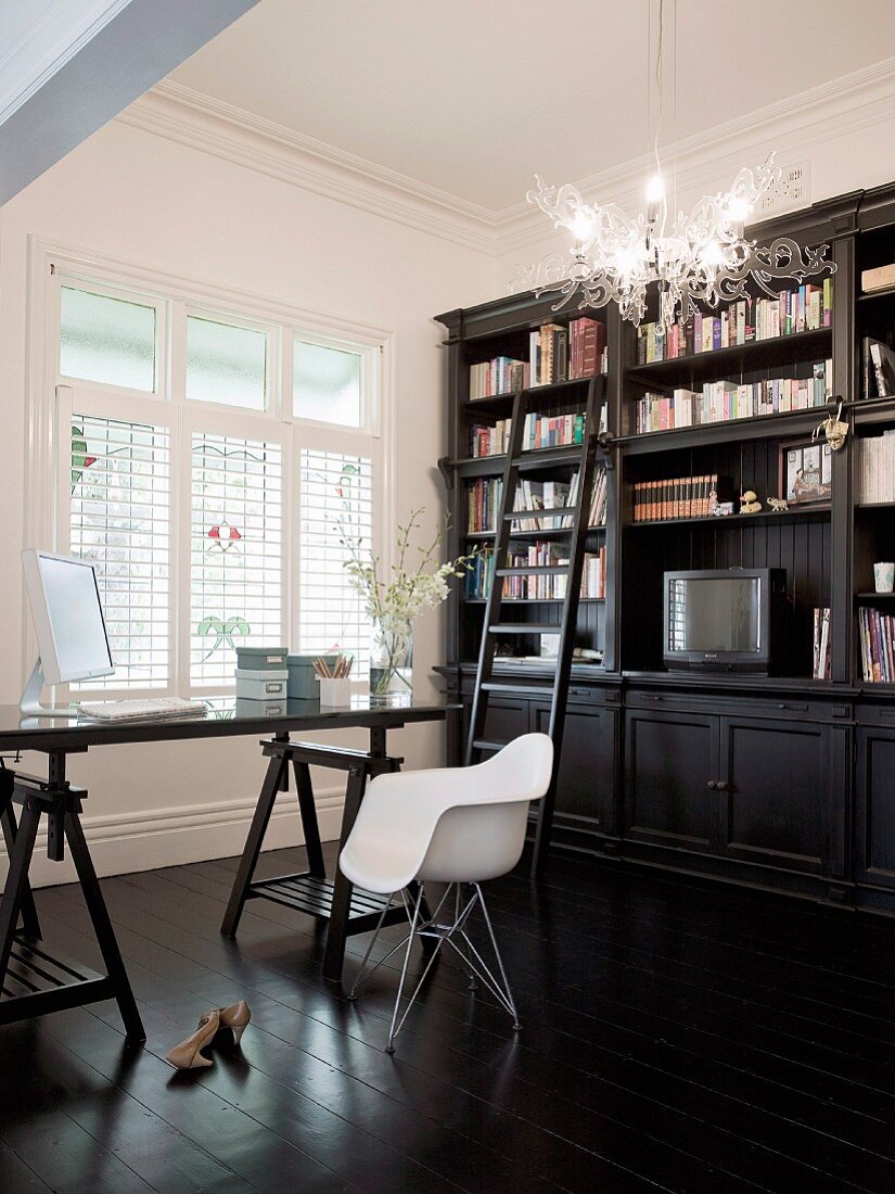 Dark furniture in study - desk on trestles, classic chair and country-house bookcase behind plexiglass lamp